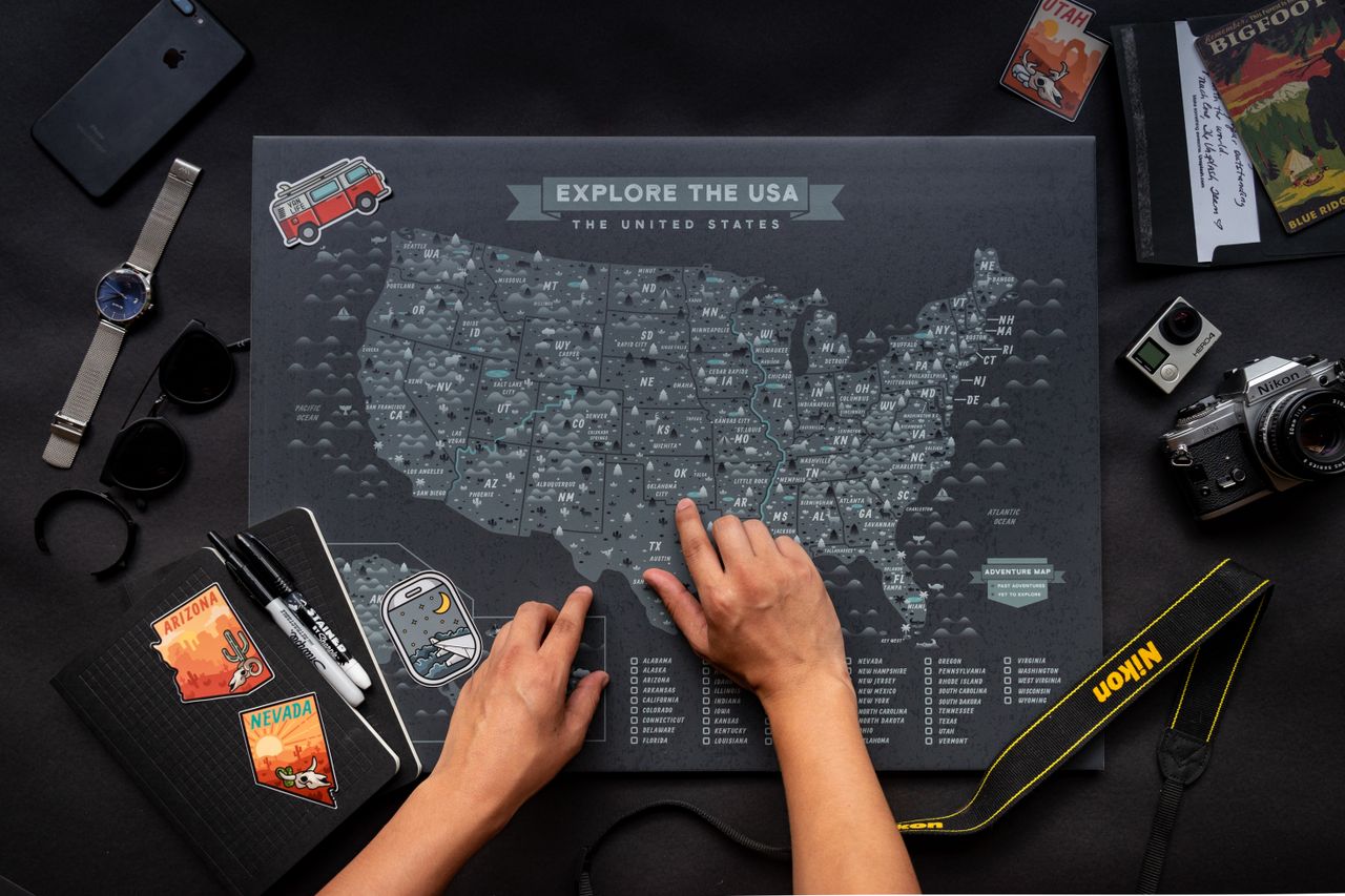 Hands interacting with a USA map alongside travel essentials including a notebook and camera.