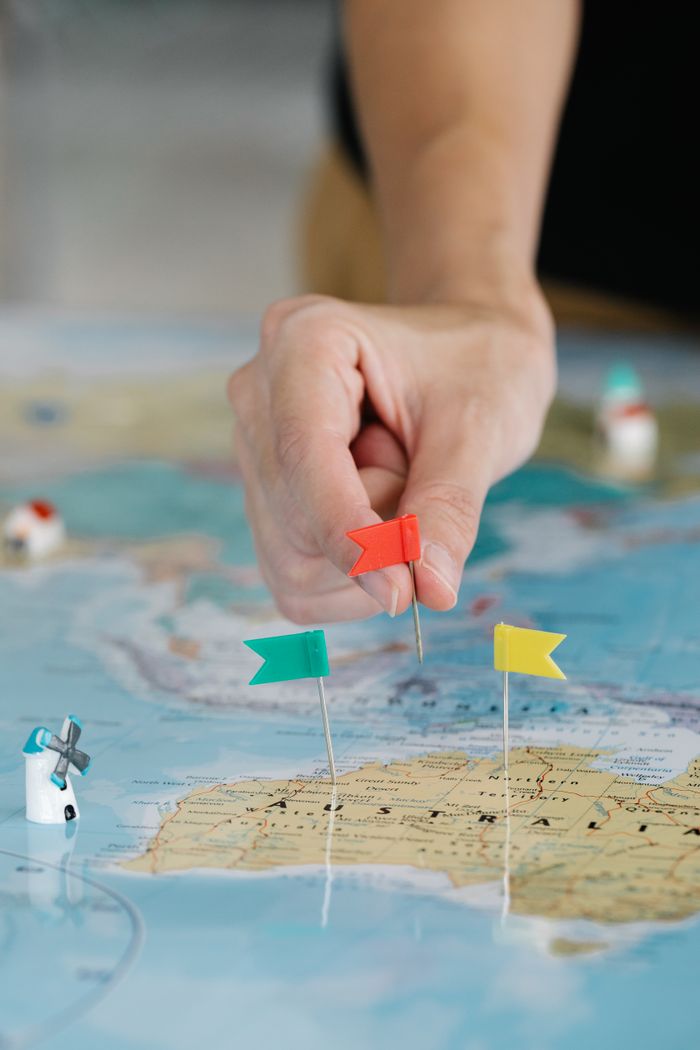 Close-up of a hand pinning flags on a map for trip planning and exploration.